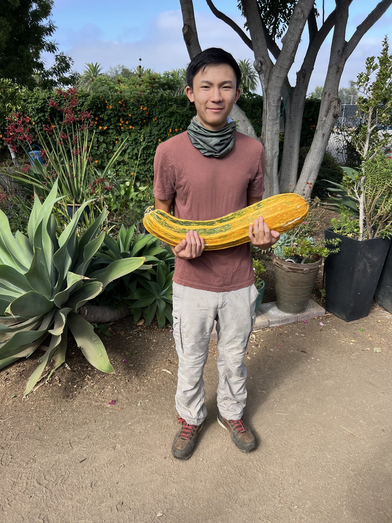 A smiling volunteer holding a large squash grown at the Farm + Food Lab