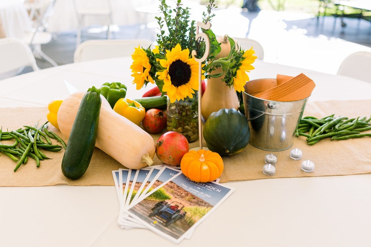 Close-up of harvest produce centerpiece with sunflowers and event brochures