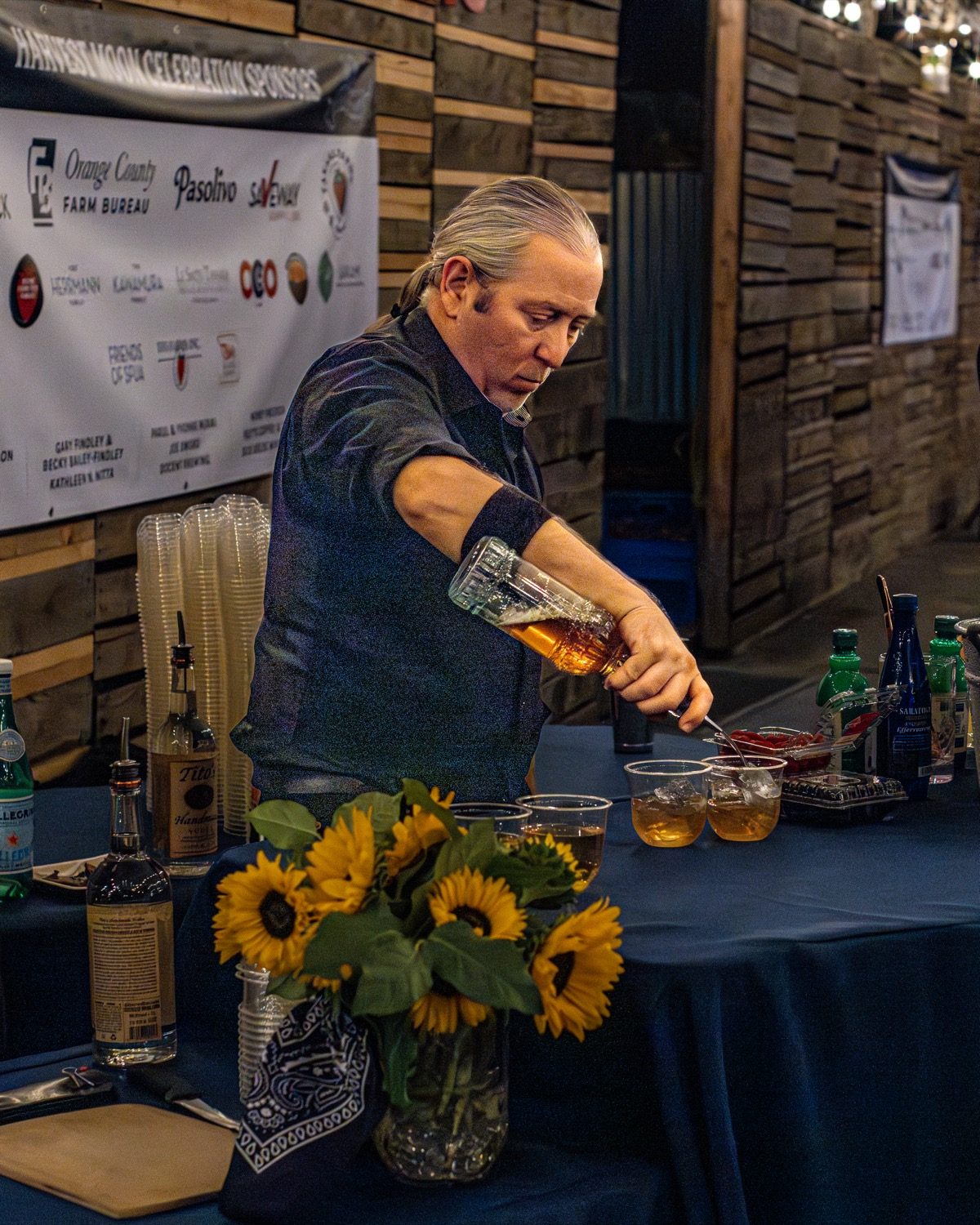 Bartender pouring drinks beside sunflower arrangements at Harvest Moon