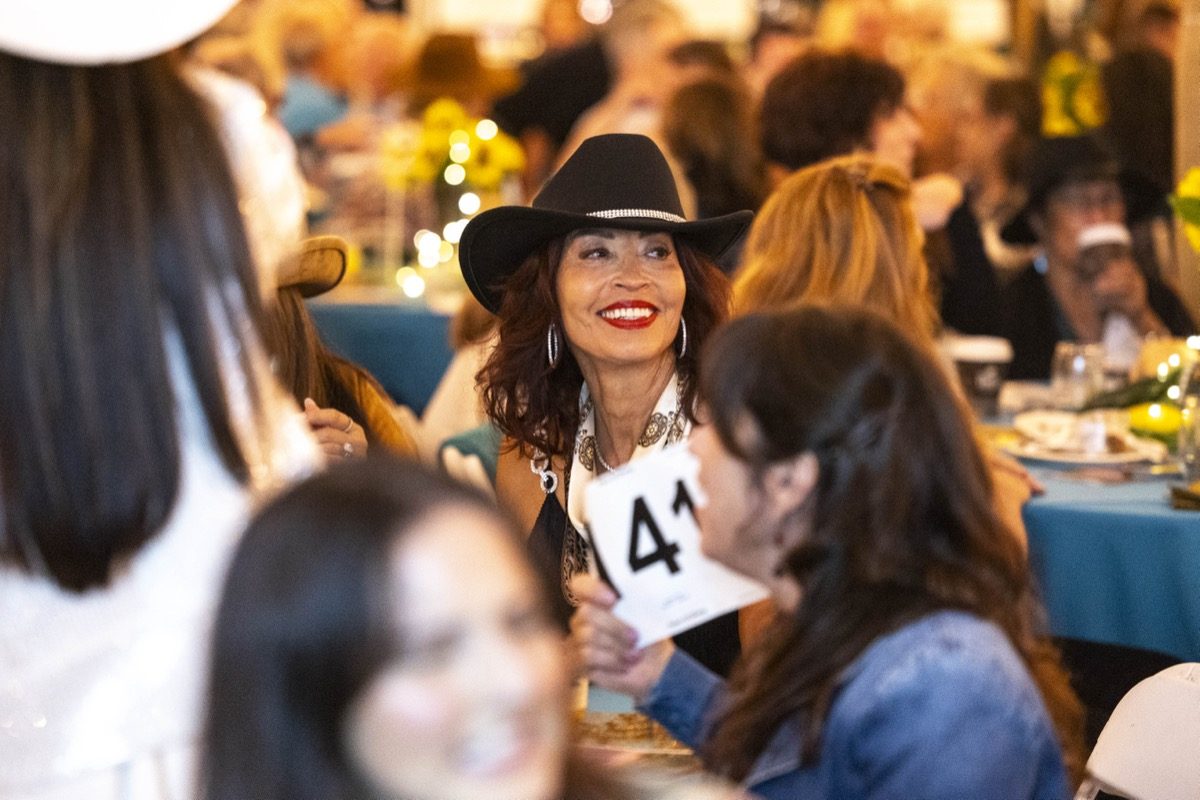 Smiling guest in cowboy hat holding auction paddle at Harvest Moon